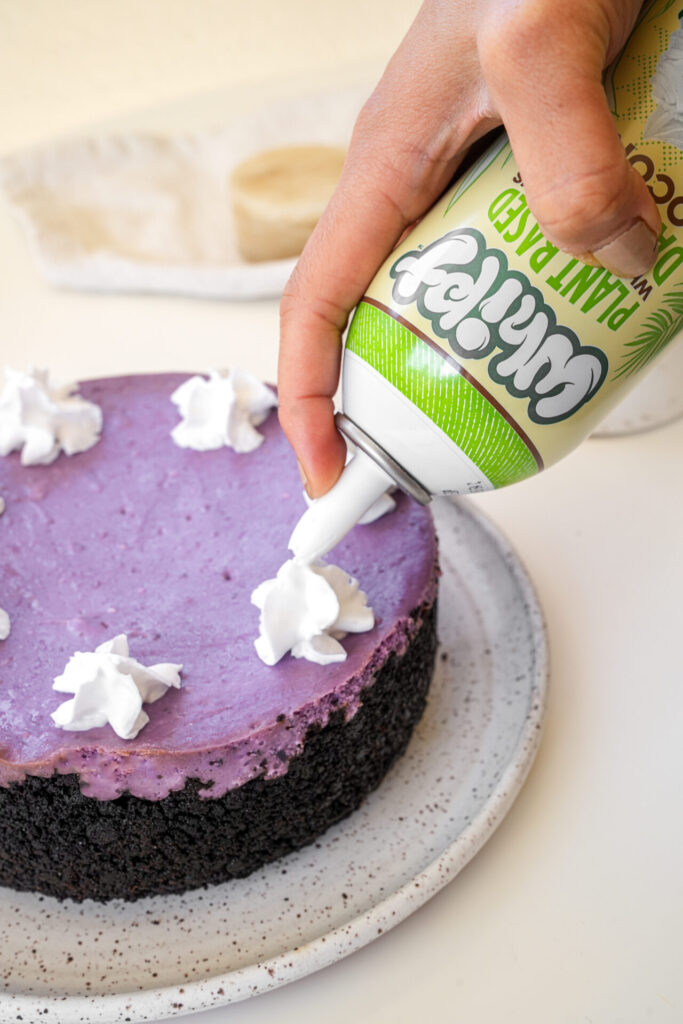 adding whipped cream topping to ube cheesecake