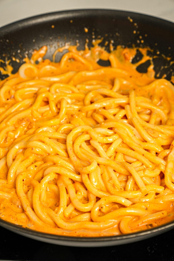 add cooked udon noodles to the pan and coat them evenly with the sauce